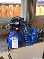 View of blue air compressor tank with black motor housing and attached blue coiled air hose.