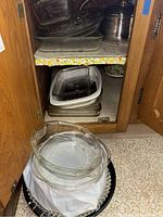 Open kitchen cabinet showing stacked glass bakeware and metal baking pans stored inside with a large stainless steel pot to the right.