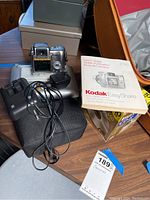 Kodak EasyShare digital camera Z740, user manual, black padded carrying case, charger cable, and part of docking station visible.