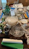 Wide view of all items on lace tablecloth including glass bowls, cups, candle holders, and decorative flowers