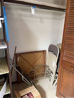 Folding card table leaning against wall with folding chairs stacked nearby, showing size and condition