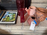 Clay planters, glass vase, and paintings grouped together on a ledge showing condition and details