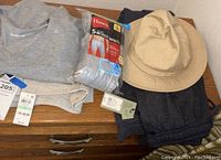 Photo showing the clothing items laid on wooden surface, including the tan bucket hat, dark pants, grey fleece pants, and a package of Hanes boxer briefs.