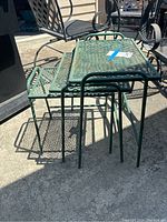 Set of 3 small green metal stacking tables viewed from the side showing how they nest inside each other.