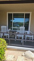 Three white plastic chairs and a small round glass-top side table on a patio.