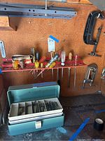 Photo showing a metal box organizer containing various sized screws, multiple screwdrivers on a red rack, and some metal hardware pieces mounted on a corkboard.