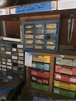 View of stacked plastic and metal small parts storage drawers with labels, containing screws and drill bits.