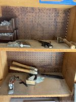 Photo of storage shelf containing hammer, scissors, pruning shears, garden shears, and other tools arranged on pegboard backing