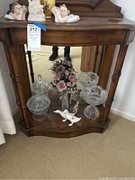 Photo showing wooden shelf with crystal candy dishes, two white duck figurines, floral arrangement, and white figurine.