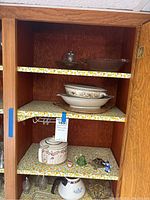 Photo of three shelves showing teapot, salt and pepper shakers, platters, bowl, and small figurines inside a wooden shelf cabinet