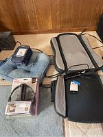 Photo showing all items together: blue blood pressure cuff, Homedics seat comfort pad with attached controller, and boxed headphones.