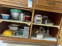 Wide view inside kitchen cabinet showing multiple plastic bowls, glass containers, graters, and mixer base.