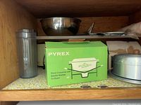Wooden shelf with metal mixing bowl, Pyrex box labeled 'Floral Casserole with Candle Warmer 1 1/2 Quart', and a round metal baking mold.