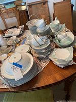 Wide shot of numerous Noritake China dinnerware pieces arranged on a wooden table, including plates, bowls, teacups, and serving dishes.