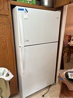 Front and angled view of white Whirlpool top-freezer refrigerator in kitchen surrounded by wooden cabinetry.