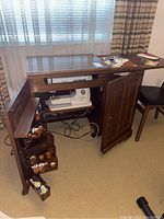 Full view of Viking sewing machine in dark wood cabinet with one door open showing thread compartments and sewing items.