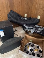 Speakers, carrying bag, and box of Chevrolet hubcaps on floor with wood panel background