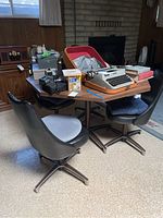 Four black vinyl swivel chairs with grey cushions around wooden table, typewriter and miscellaneous items on table.