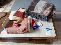 Overview of items on a wooden table including woven throw blanket, crochet piece, ruffled fabric tray, bandana.