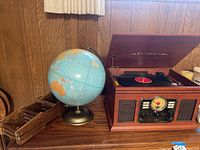 Photo showing Victrola turntable radio with lid open, blue globe, wooden crate on wood cabinet against wood-paneled wall