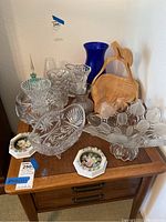 Glass vases, crystal bowls, wooden cutting boards, and porcelain decorative pieces arranged on a table.