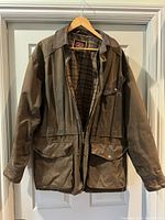 Full front view of brown leather coat hanging on a hanger showing front pockets and collar.