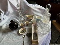 Wide view showing entire lot including decanters, bowls, china cups, silver spoon, trinket box, and small glass bottle.