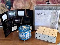 Lot items displayed on table: black multi-photo frame, vintage blue footed tin, unopened hanging closet organizer packaging, white studded wooden box closed.