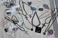 Overview of multiple crystal necklaces, earrings, and accessories laid out on fabric. Includes black cord necklaces with various crystal pendants and some items in plastic bags.