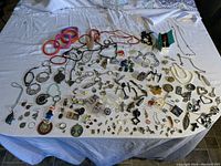 Wide layout of the entire jewelry collection on a white cloth, showing various pins, rings, necklaces, earrings, and bracelets arranged spread out.