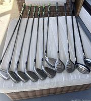 Full view of the golf clubs laid out on a white surface showing irons and woods with graphite shafts and grips.