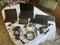 Full view of lot on table showing laptops, keyboards, tablet, power adapters, and cables
