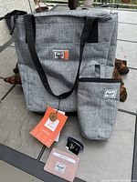 Photo of the Herschel tote bag, water bottle cooler pouch, card wallet and wrist bracelet arranged on a table, with tags visible.