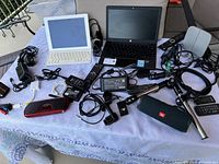 Overview of all items on table including Chromebook, iPad, speaker, selfie stick, chargers, remotes, and cables.