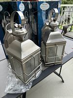 Pair of new Canarm outdoor wall lanterns with brushed pewter finish shown with original packaging and all mounting hardware included.