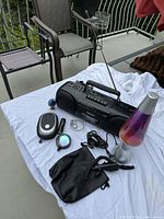 Full lot view showing Panasonic cassette radio, lava lamp, Bluetooth speaker, small flashlight, earphones, cables, and decorative figurine on white cloth.