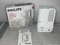 Philips TS8000 travel garment steamer next to its original box and instruction manual on a gray surface