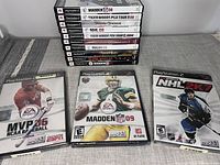 Stack of 10 PlayStation 2 game cases showing titles including Madden NFL 08, Madden NFL 09, NHL 08, Tiger Woods PGA Tour 08, Pirates of the Caribbean, Rugby 06, Tetris Worlds, and others.