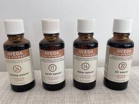 Four amber glass bottles labeled as Aveda Key Element essential oil blends: Infinity Nature 24, Earth Nature 11, Water Nature 14, Air Nature 22. Each is 1 oz with white screw caps, standing upright.