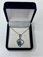 Sterling silver heart-shaped pendant featuring an oval blue-green Australian black opal stone at the center, attached to a delicate sterling silver chain, presented inside a black velvet jewelry box with white satin lining.