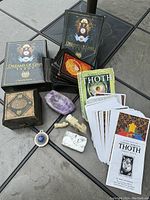 Photo showing two tarot decks: Dreams of Gaia and Aleister Crowley Thoth, alongside a small amethyst bowl, two carved stone figures, a decorative wooden box, a small tin box, and a colored metal case with stone clasp.