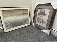 Pair of framed artworks on the floor showing both art pieces. One is a landscape and the other a portrait, both matted and behind glass.