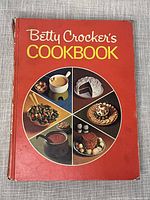 Front cover of the vintage Betty Crocker's Cookbook featuring red background and circular food images.