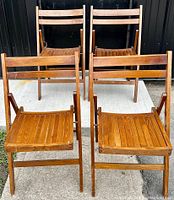 Four vintage wooden folding chairs arranged in two rows, front two chairs open and rear two chairs partially shown folded or standing, on concrete surface.