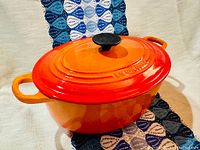 Front side view of orange Dutch oven with lid, showing Le Creuset embossing and loop handles