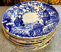 Stack of twelve luncheon plates angled to show blue and white oriental Mikado pattern and gilt rims