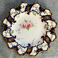 Top-down view showing the full scalloped edge, cobalt blue panels, gold gilt accents, and detailed pink rose floral pattern at center.