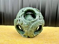 Front view of the green soapstone puzzle ball showing carved dragon and leaf details with visible layered structure.