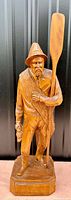 Front view of large wooden fisherman sculpture holding an oar and small boat with detailed carving and natural wood finish.