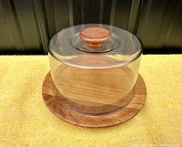 Side and angled view of the cheese keep showing the teak wood base and clear plastic dome cover with wood knob.